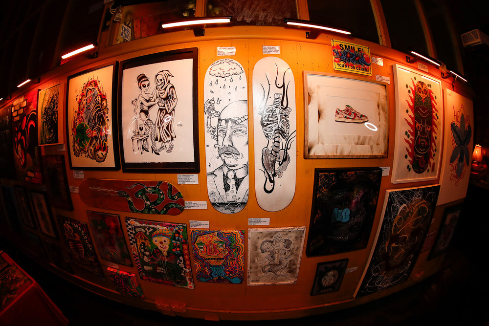 Framed artworks and illustrated skateboard decks displayed on an orange wall