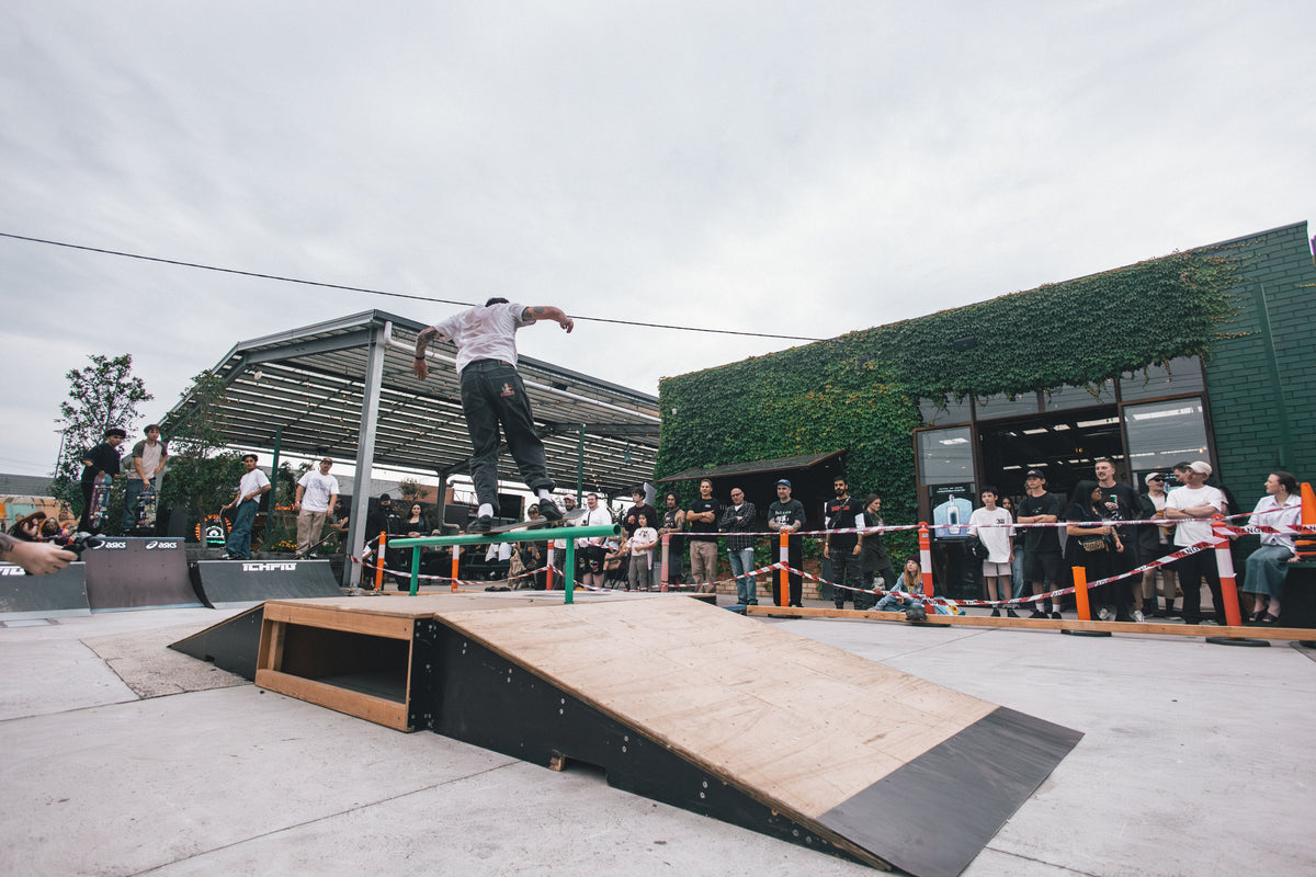 A skateboarder rides a rail above wooden ramps as spectators watch